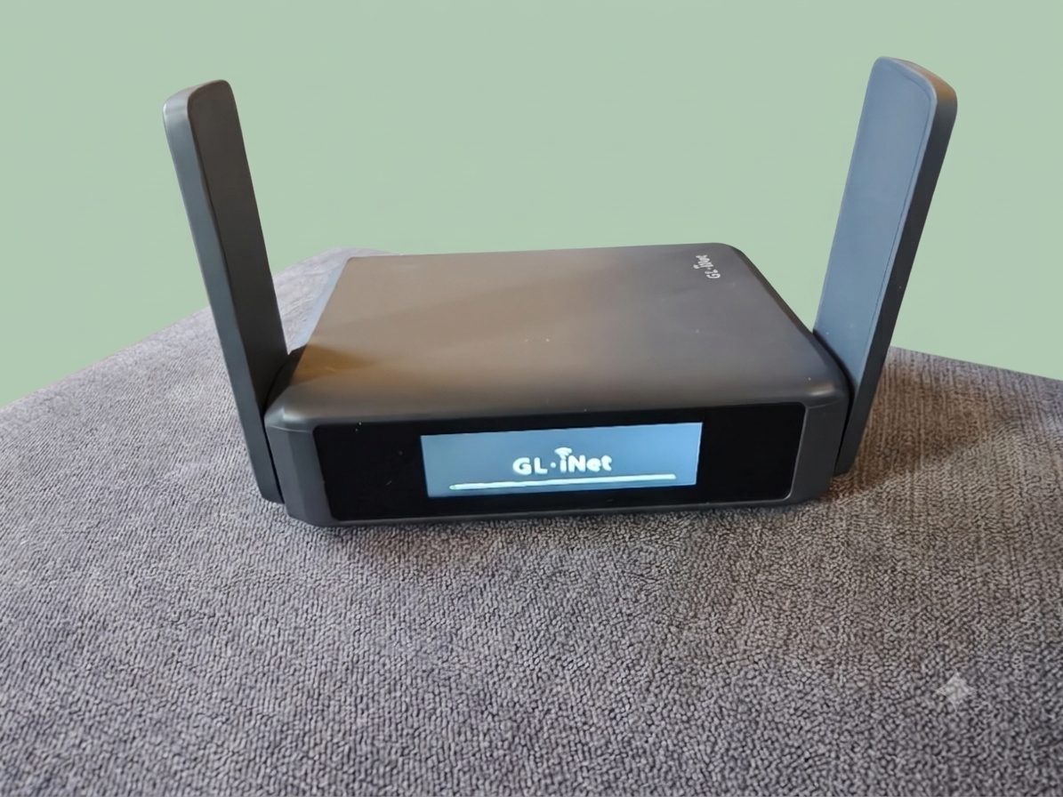 My GL.iNet Slate 7 travel router on a grey sofa arm, antennas up, with the GL.iNet logo on its front touchscreen.